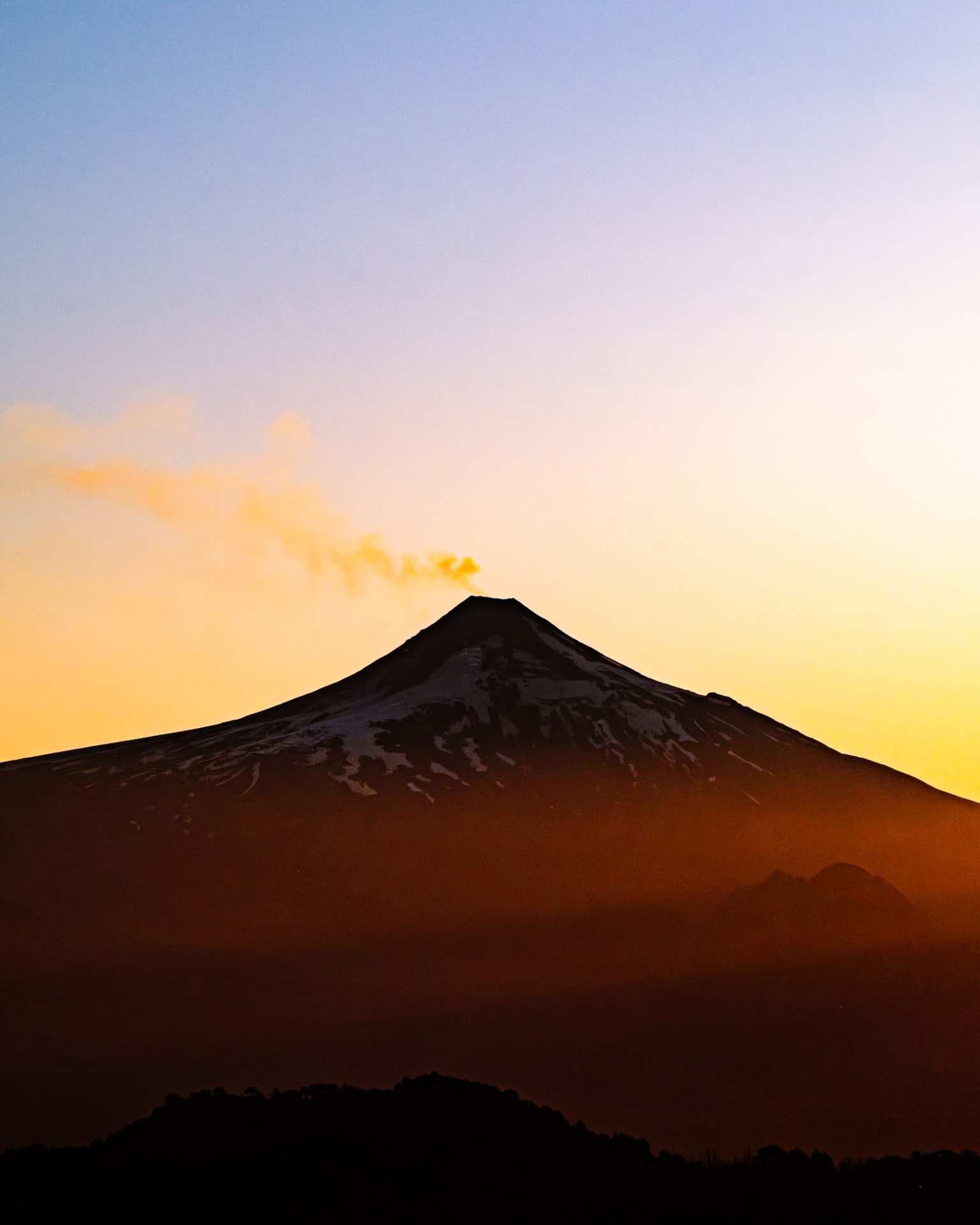 Volcán Villarrica al atardecer en tonos anaranjados y violetas, con su fumarola