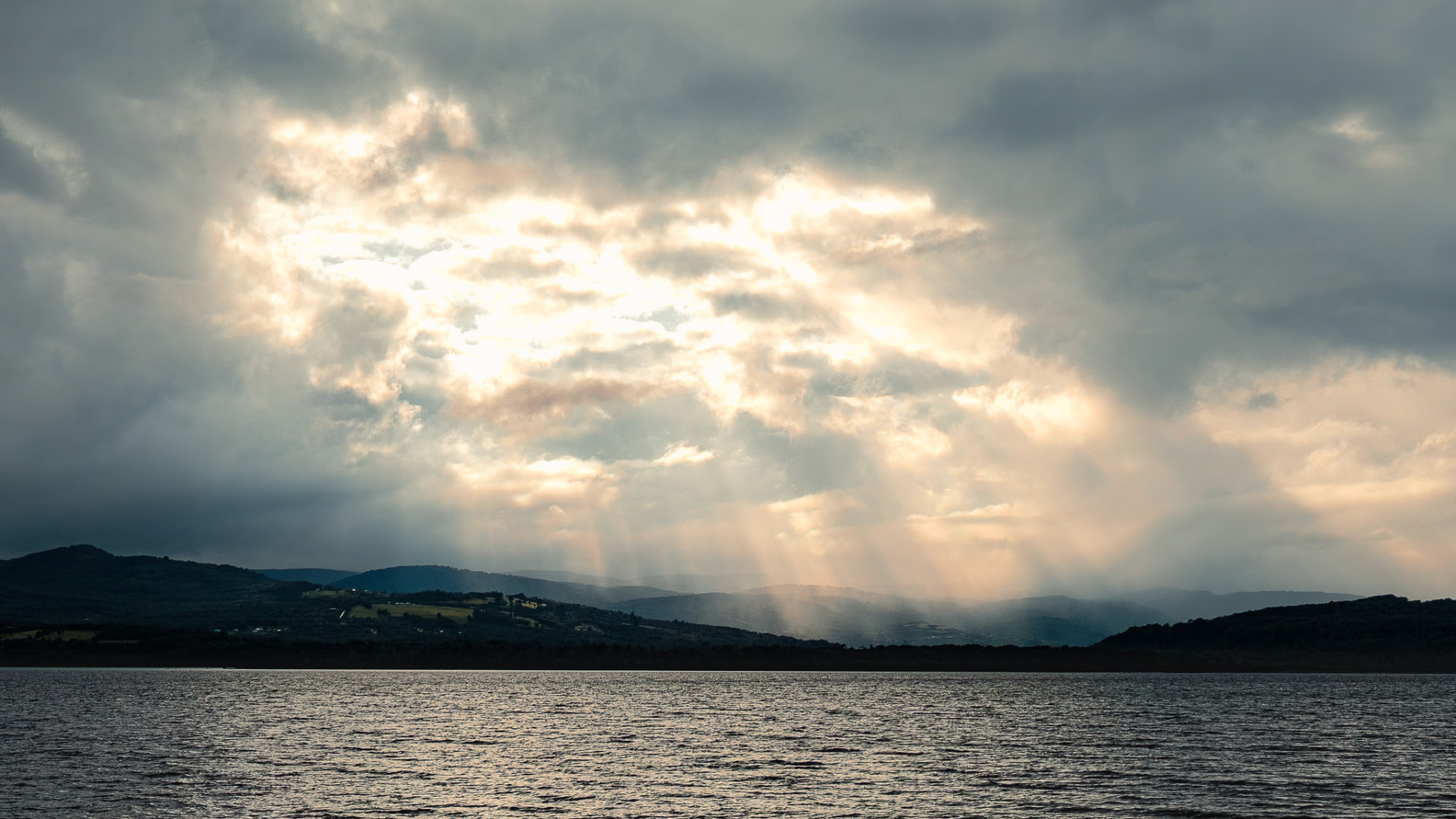 Lago y colinas verdes de Chiloé con haces de luz atravesando las nubes