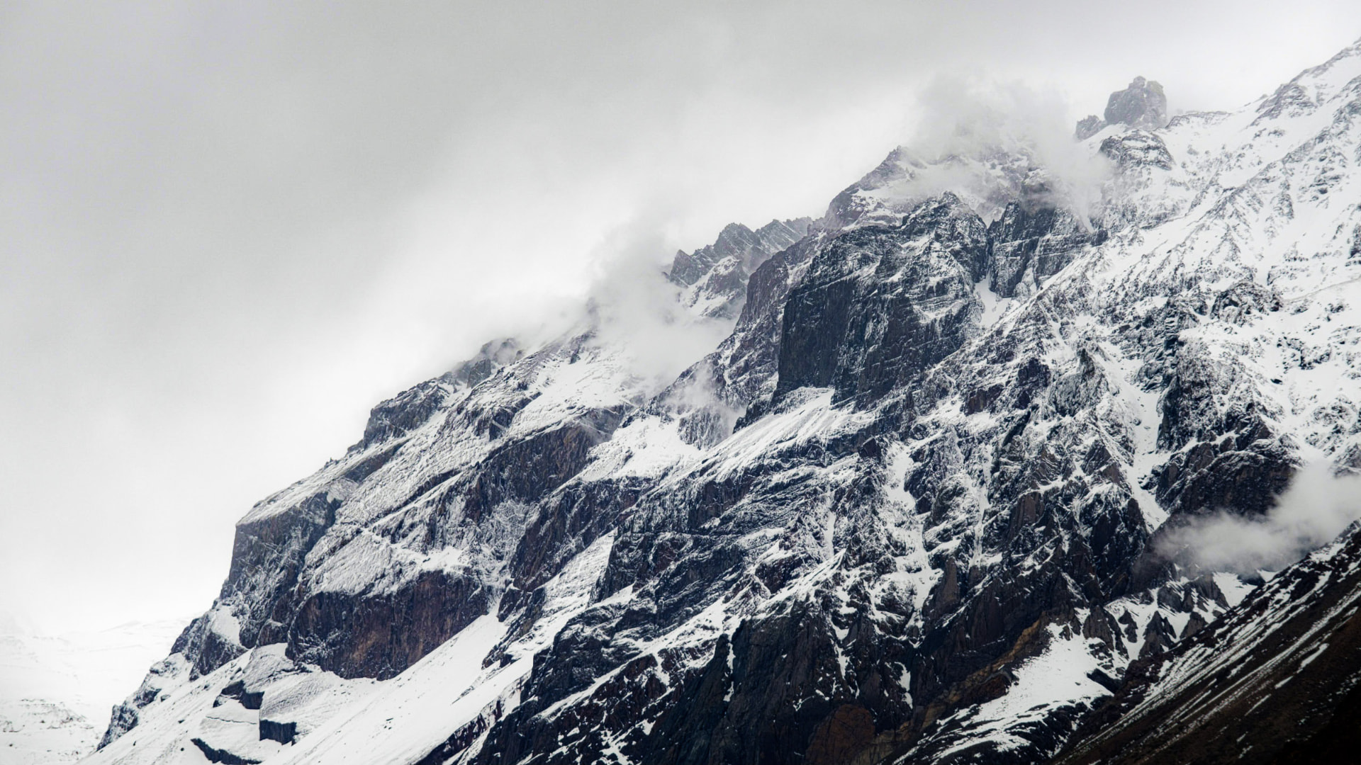 Perfil invernal de una montaña de Lo Valdés con nieve y rocas expuestas bajo un cielo nublado