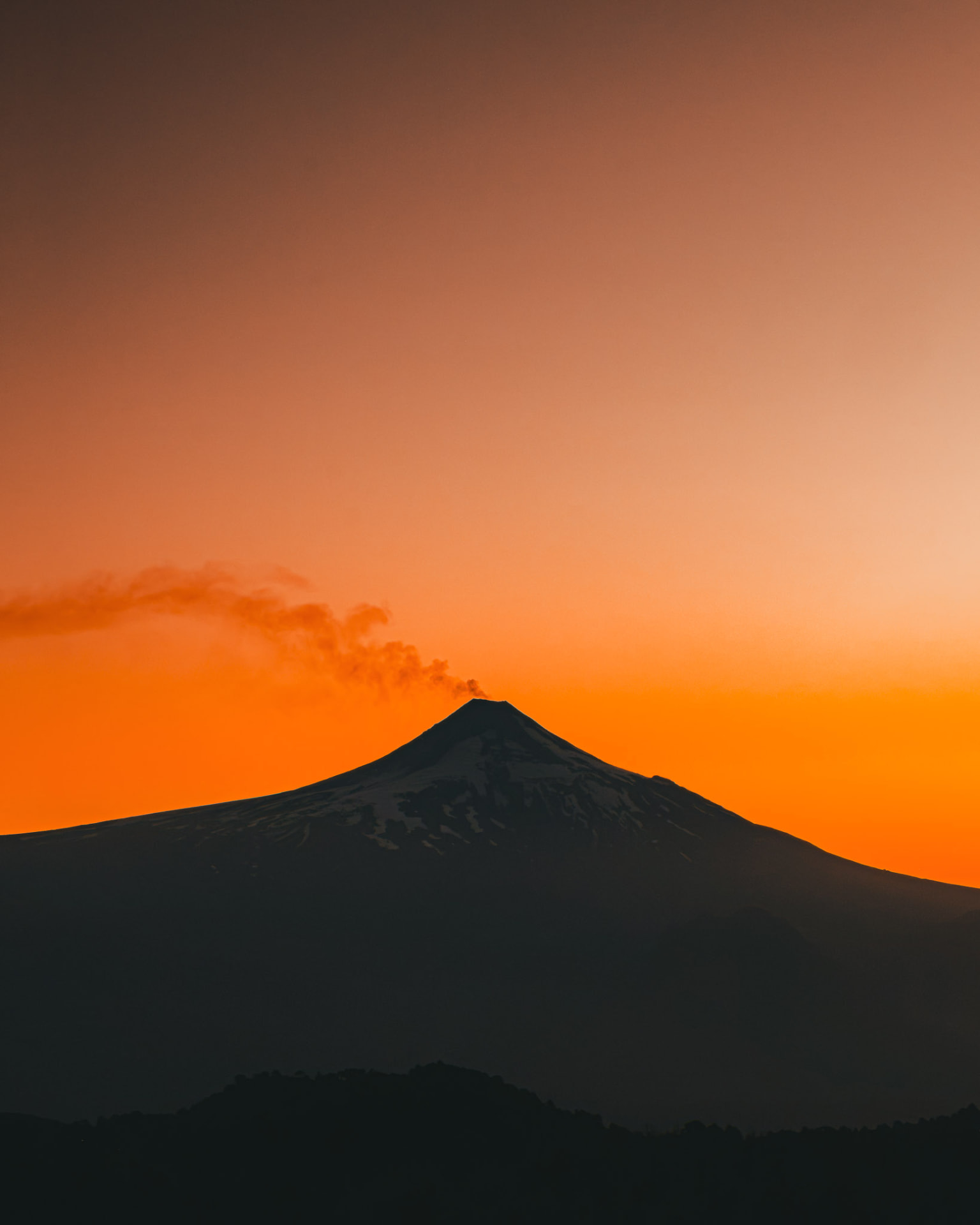 Volcán Villarrica al atardecer con cielo anaranjado y su fumarola visible